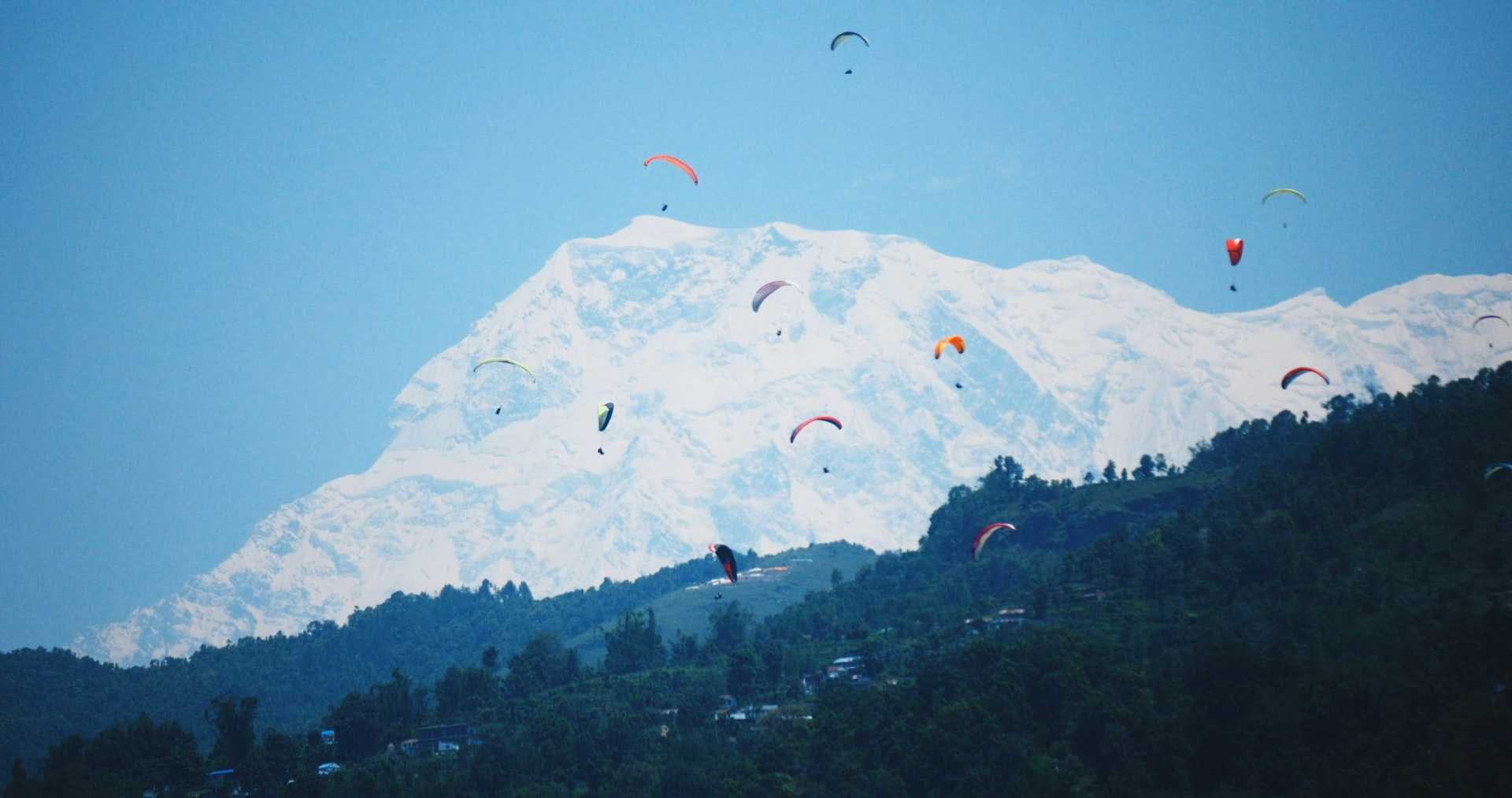 Paragliders on the sky, snow capped mountains on the background.