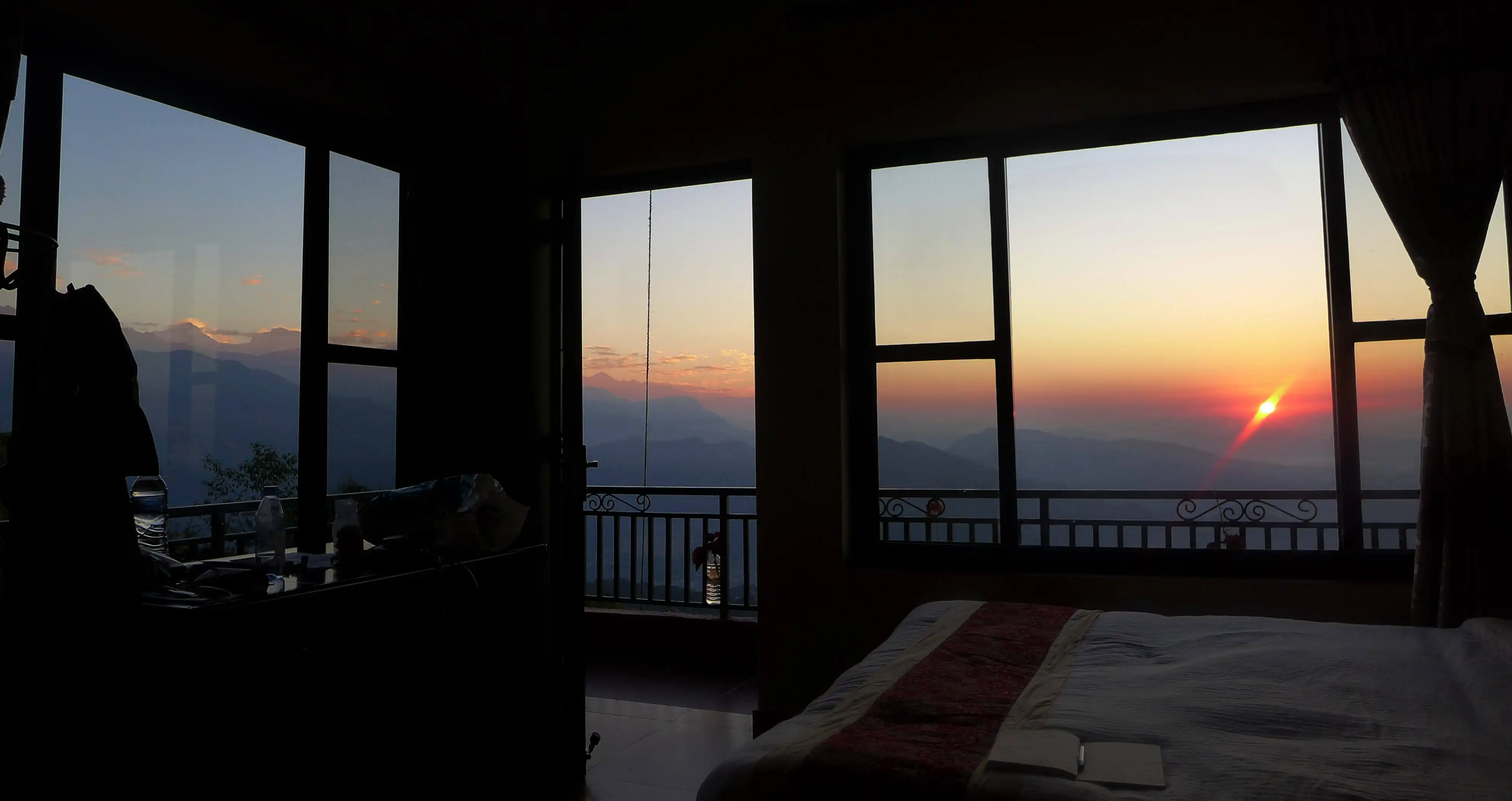 sunrise seen from the windows of a room with neatly bed room with table on a side