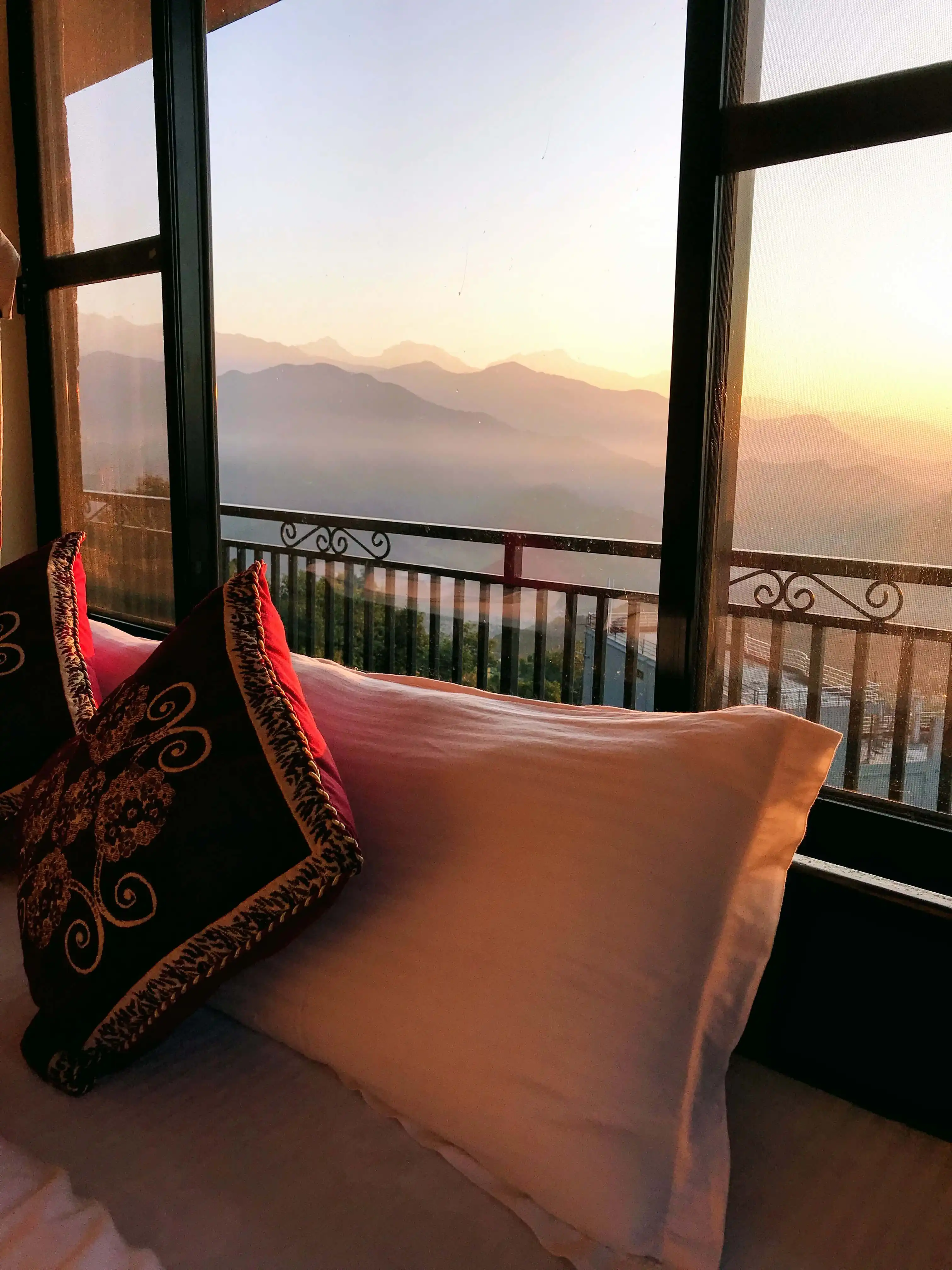 Bed top golden with sun beams, mountains seen from large window beside bed